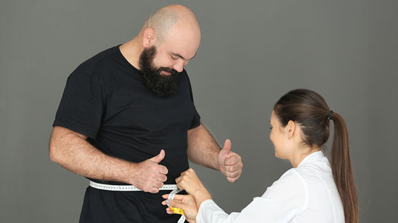 Male patient having waist measured by female physician.